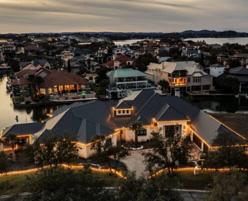 Aerial view of a lakefront home with roofline and lawn edge Christmas lights