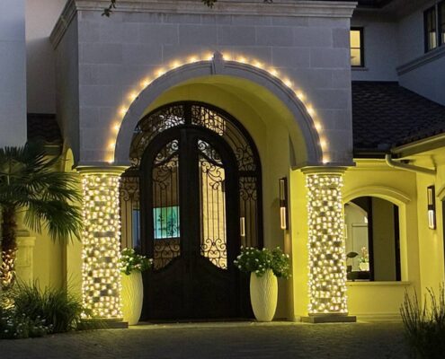 Arched front entry outlined in C9 bulbs with columns wrapped in Christmas lights
