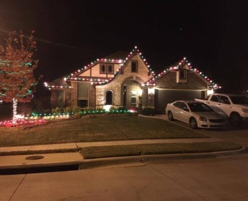 Brick home with red and green Christmas lights and a wrapped yard tree