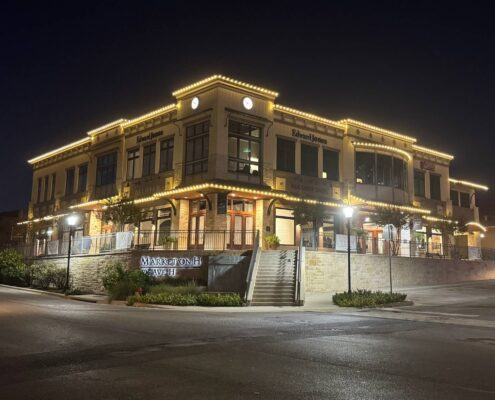 Two-story commercial building outlined in warm white Christmas lights at night