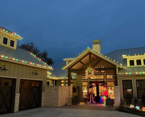 Farmhouse entry with multicolor C9 roofline Christmas lights and a wreath