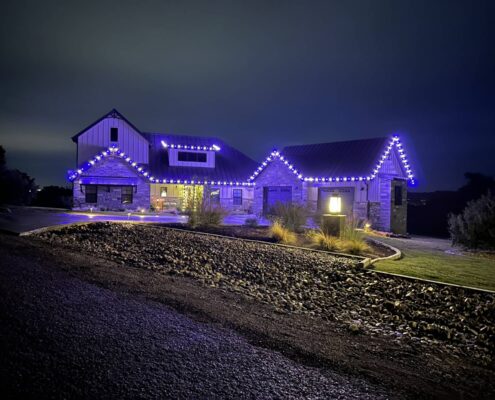 Stone farmhouse outlined in purple LED roofline lights at night