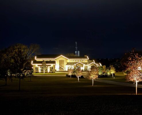 Ranch estate outlined in white Christmas lights with lit trees across the lawn