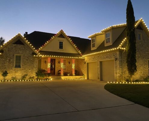 Stone two-story home with warm white roofline lights and wrapped porch columns