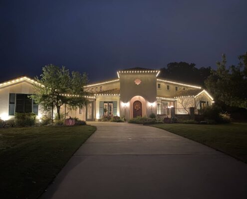 Stucco home with warm white roofline Christmas lights at dusk