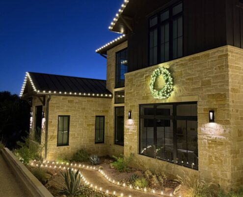 Path lights along a garden walkway with roofline Christmas lights and a wreath above