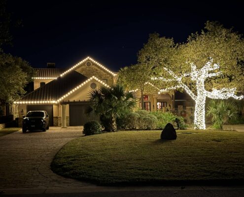 Home with white roofline Christmas lights and a brightly wrapped live oak